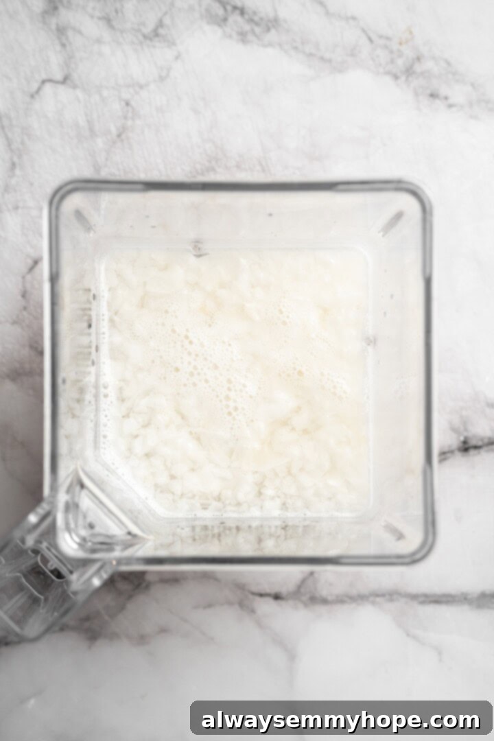 Unsweetened coconut flakes and room temperature water inside a high-speed blender, ready to be processed.