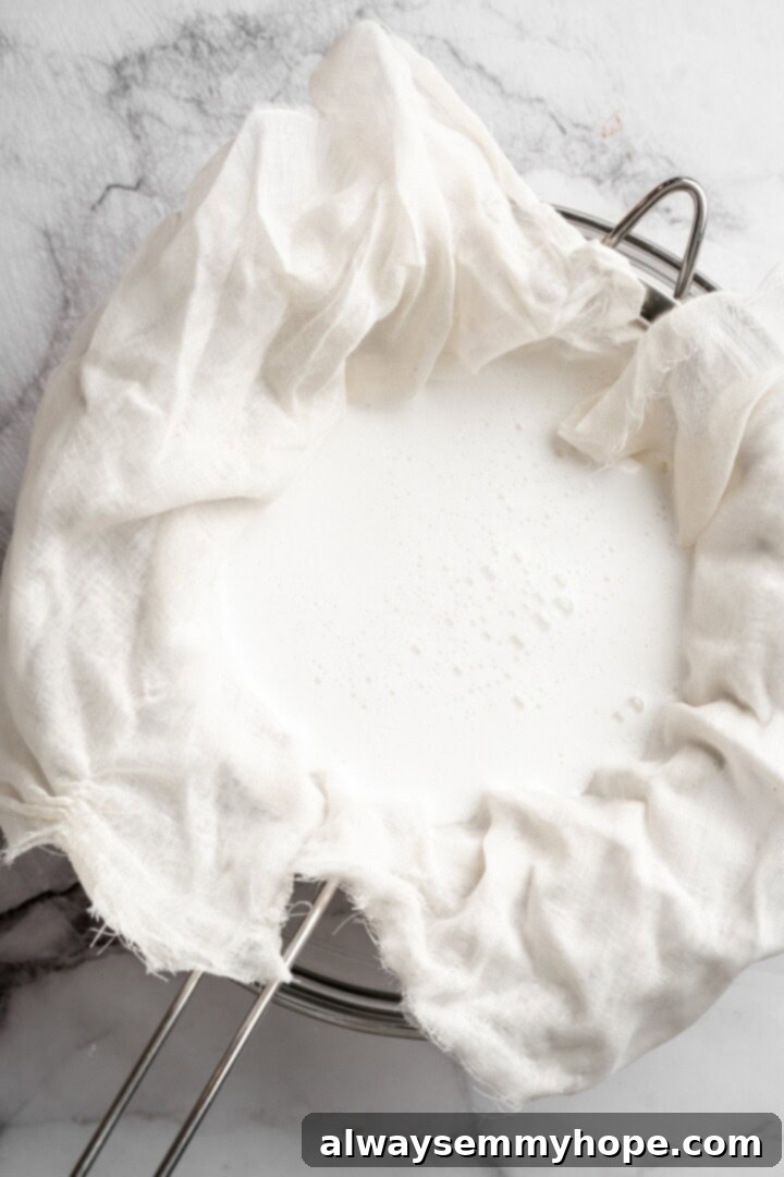 Straining homemade coconut milk through a fine cheesecloth into a glass bowl, separating the liquid from the coconut pulp.