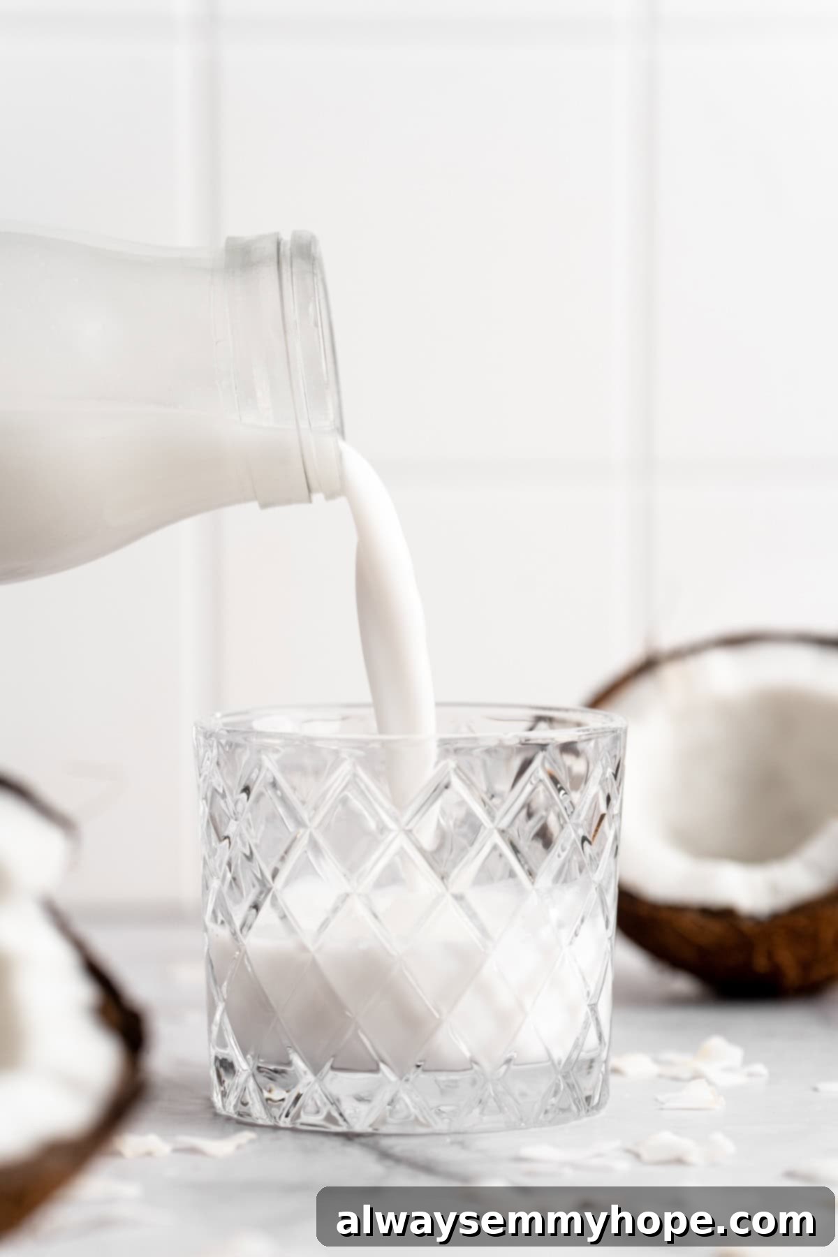 A hand pouring freshly made homemade coconut milk from a glass bottle into a clear glass.