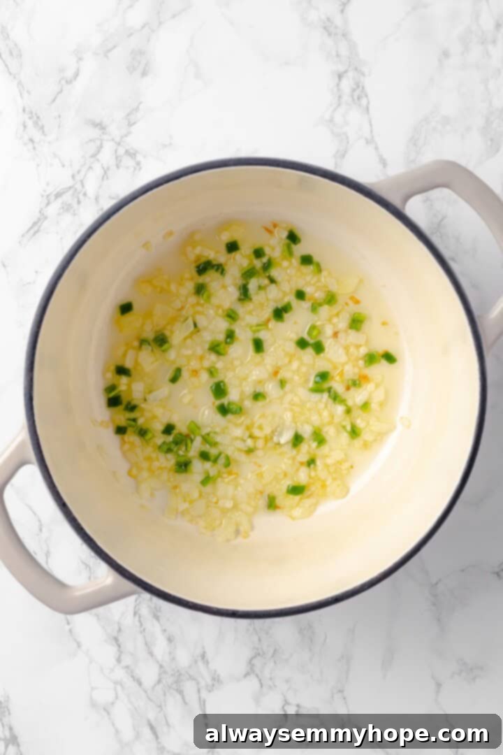 This vegan enchilada soup recipe has the flavor of enchiladas in a hearty bowl of soup. Loaded with beans, plant-based chicken and more! Overhead view of diced onion, minced garlic, and finely chopped jalapeño cooking in olive oil in a Dutch oven