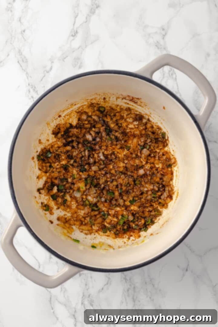 This vegan enchilada soup recipe has the flavor of enchiladas in a hearty bowl of soup. Loaded with beans, plant-based chicken and more! Overhead view of ground cumin, chili powder, smoked paprika, dried oregano, salt, and black pepper being stirred into the sautéed aromatics in a Dutch oven