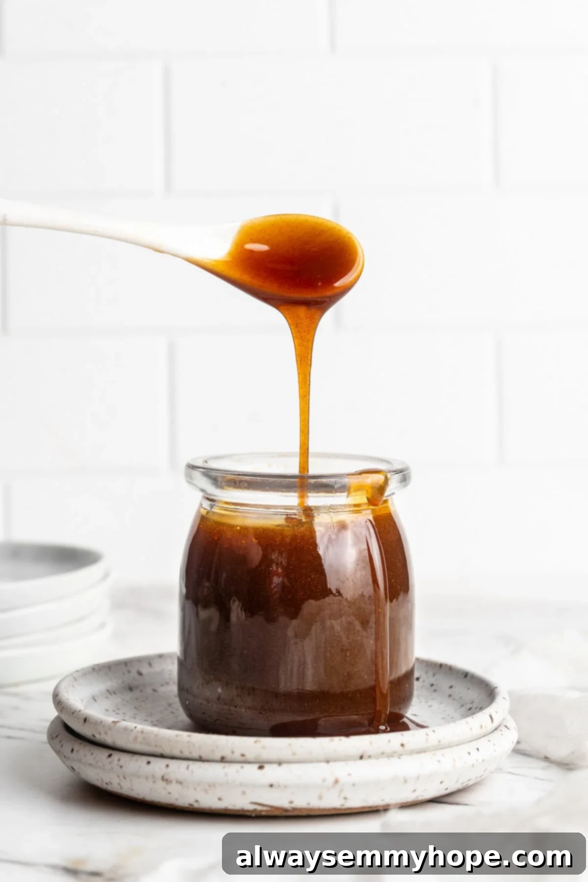 A spoon expertly drizzling thick, dark homemade date syrup into a glass jar for storage