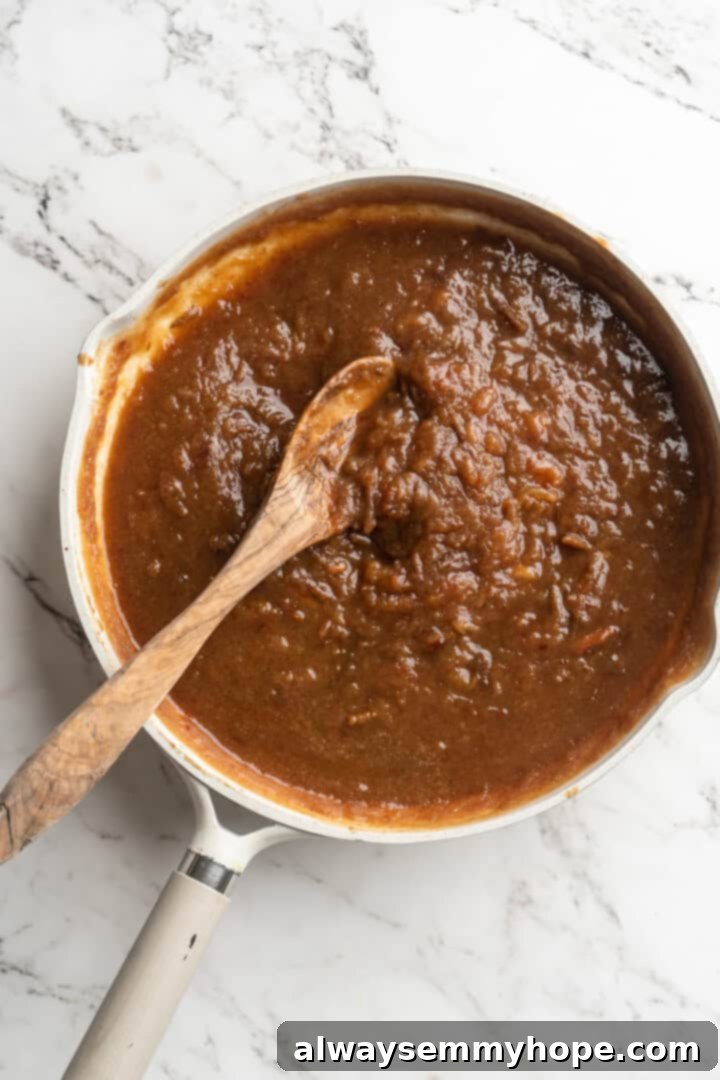 Overhead view of cooked-down dates and liquid in a pan, mashed into a loose applesauce consistency with a wooden spoon