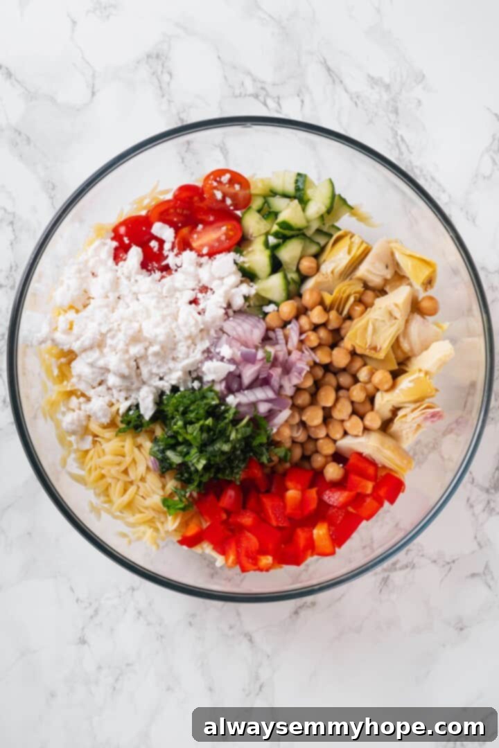 Overhead view of ingredients for orzo pasta salad in bowl before tossing