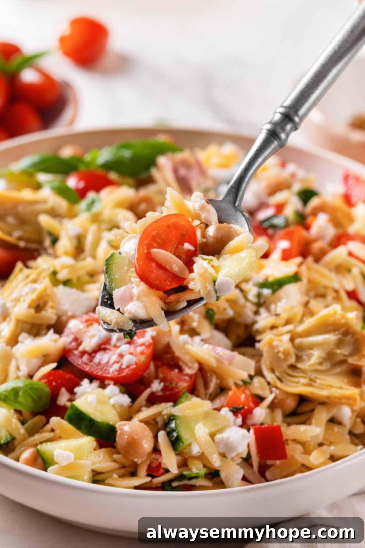 Spoonful of orzo pasta salad held over bowl