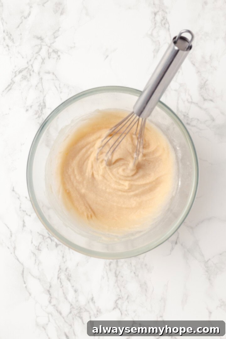 Overhead view of coconut cream, vanilla, and brown sugar mixed in bowl with whisk