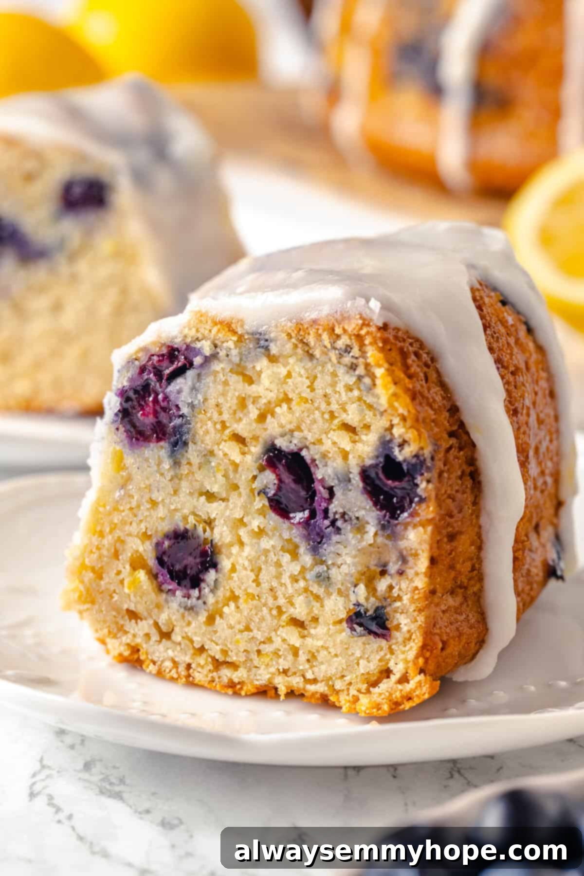 Enjoy a slice of this moist lemon blueberry Bundt cake. A close-up, dynamic shot of a single slice of lemon blueberry Bundt cake on a white plate, highlighting its texture and moistness, with a slight blur in the background.