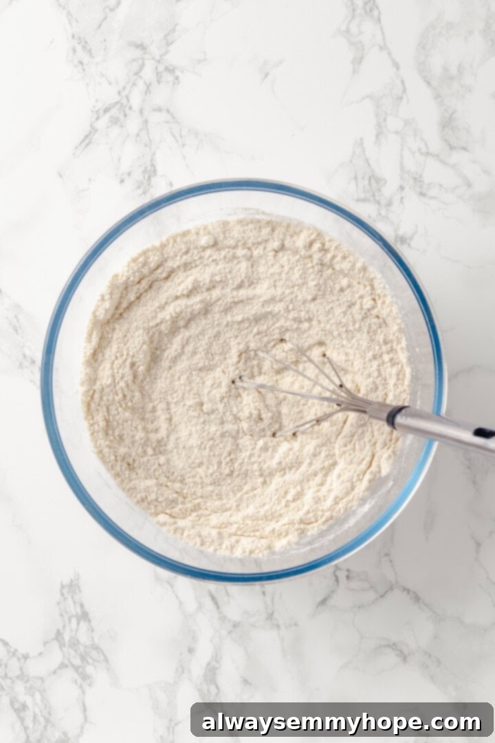 Whisk the dry ingredients for your lemon blueberry Bundt cake. Overhead shot of dry ingredients for the Bundt cake in a glass mixing bowl, being whisked together, highlighting the light texture.