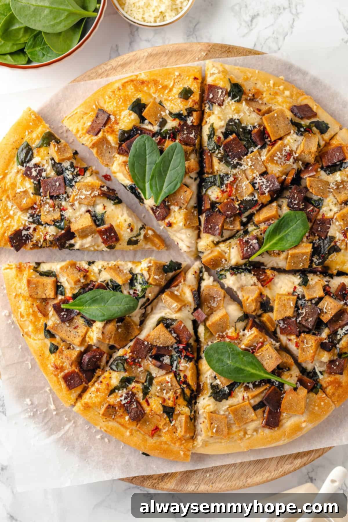 A creamy sauce makes this Alfredo sauce pizza taste indulgent, but it’s vegan! Plant-based chicken and bacon take this recipe over the top. Overhead view of whole Alfredo sauce pizza cut into slices, showcasing its creamy topping and plant-based ingredients.