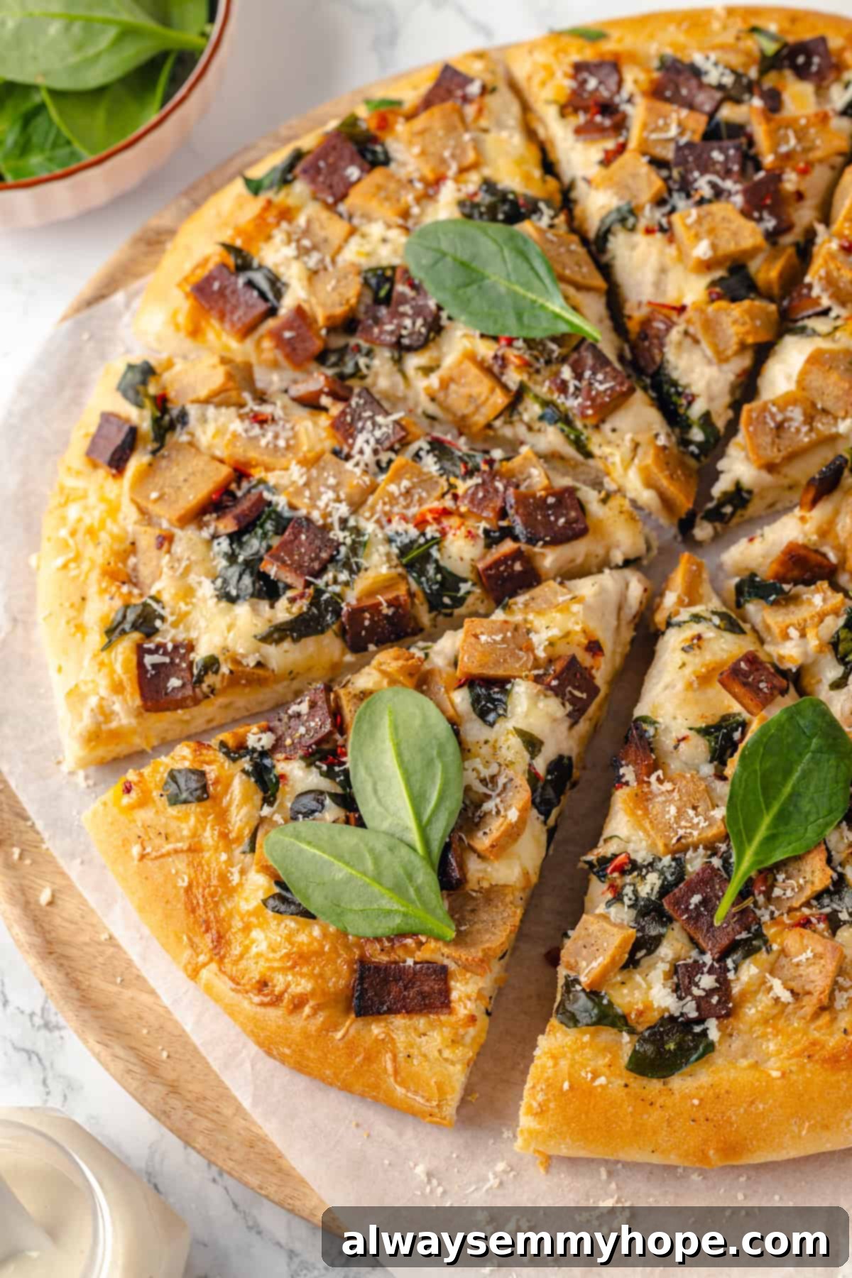 A creamy sauce makes this Alfredo sauce pizza taste indulgent, but it’s vegan! Plant-based chicken and bacon take this recipe over the top. Sliced Alfredo sauce pizza resting on parchment paper, showcasing its delicious layers.