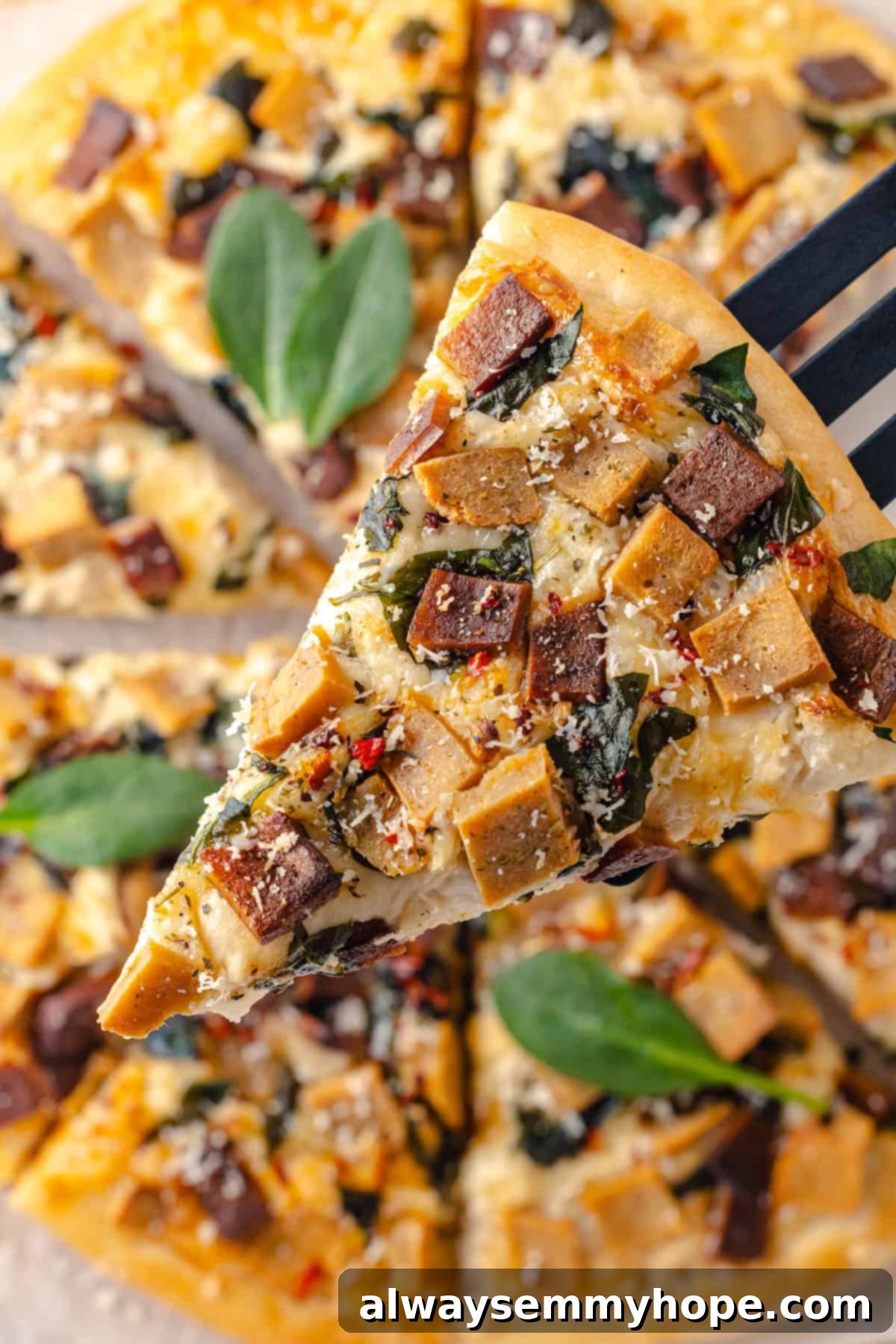 A creamy sauce makes this Alfredo sauce pizza taste indulgent, but it’s vegan! Plant-based chicken and bacon take this recipe over the top. Spatula holding a perfect slice of Vegan Alfredo sauce pizza, ready to be served.