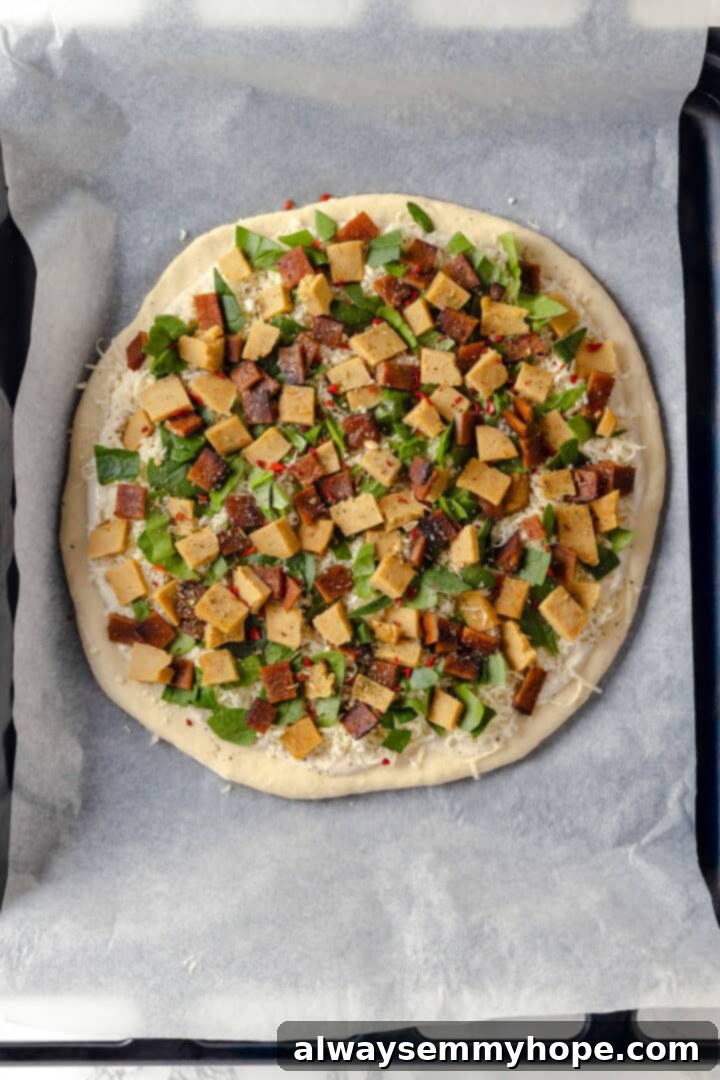 A creamy sauce makes this Alfredo sauce pizza taste indulgent, but it’s vegan! Plant-based chicken and bacon take this recipe over the top. Overhead view of a fully topped, unbaked Vegan Alfredo pizza, ready for the oven.