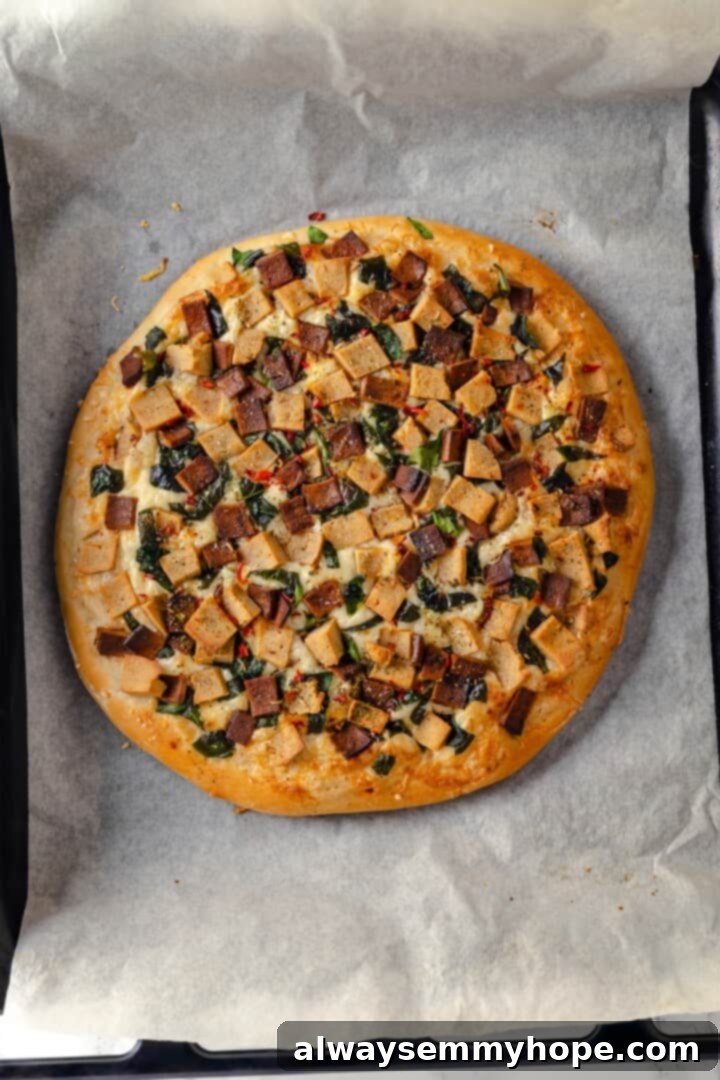 A creamy sauce makes this Alfredo sauce pizza taste indulgent, but it’s vegan! Plant-based chicken and bacon take this recipe over the top. Overhead view of a perfectly baked Vegan Alfredo pizza on parchment-lined pan, golden and bubbling.
