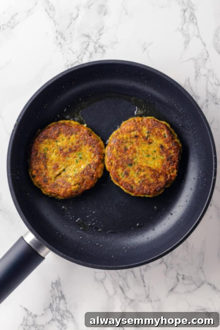 Overhead view of falafel burger patties sizzling and cooking to a golden crisp in a non-stick skillet.