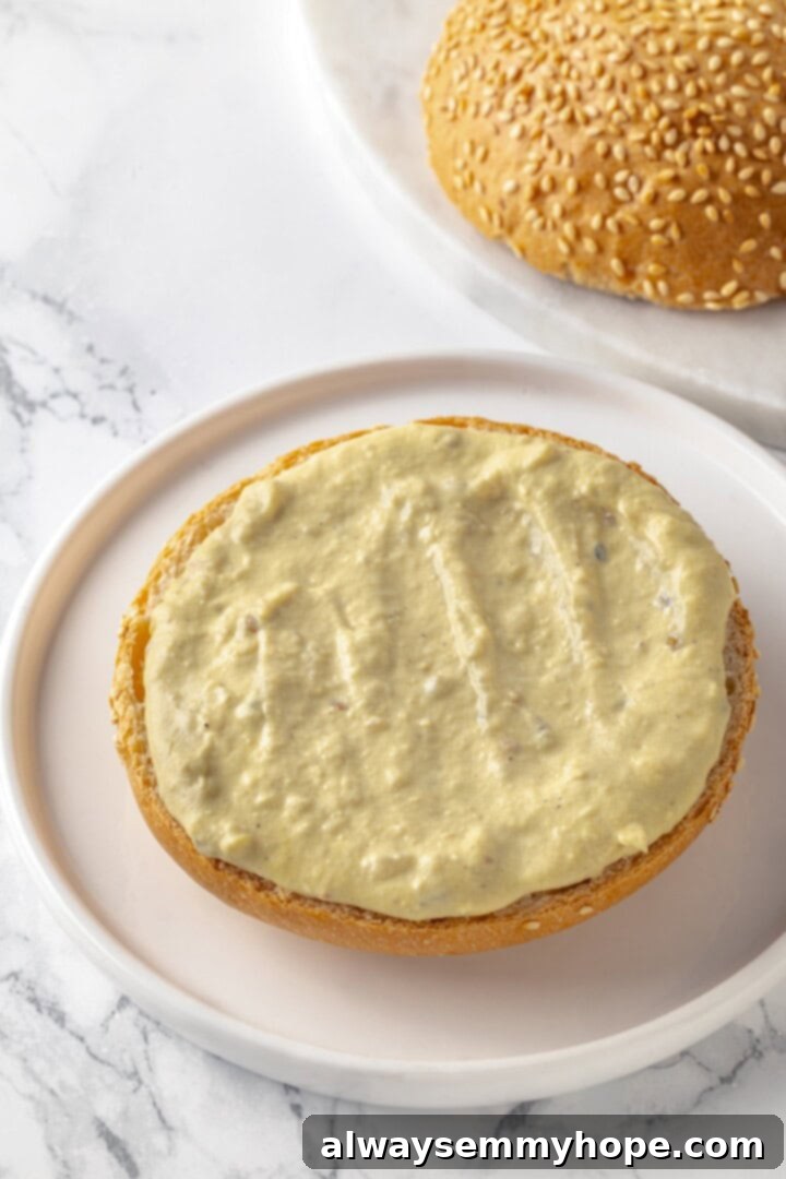 Bottom burger bun generously slathered with creamy tahini sauce, ready for toppings.