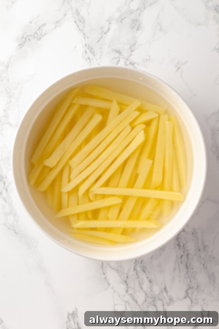 Overhead view of raw potatoes cut into fries and soaking in bowl of water