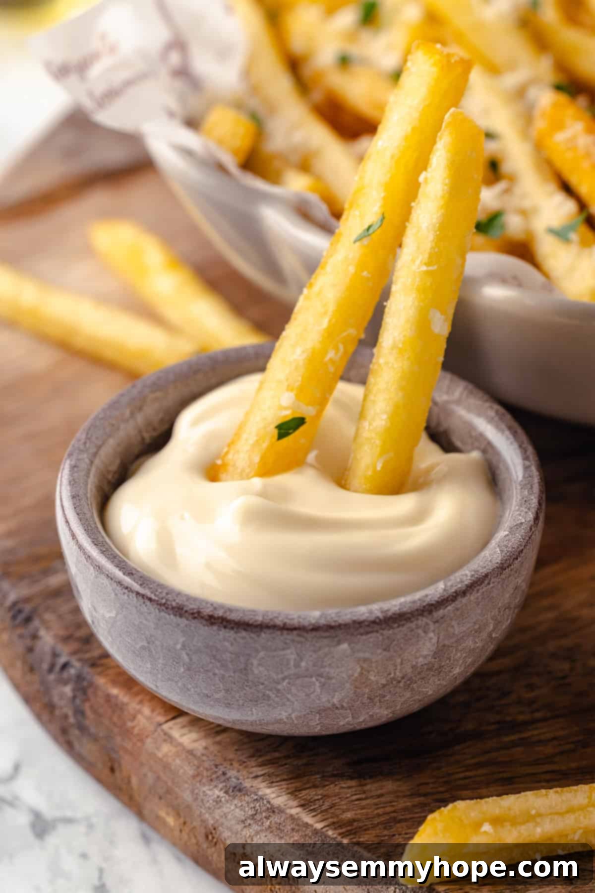 Two truffle fries dipping into bowl of aioli