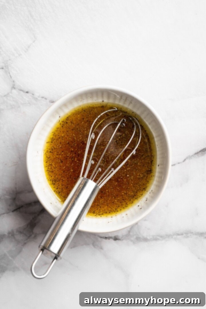 This vegan Apple, Pecan and Feta Salad is loaded with fall flavour! Sweet and crunchy, with a peppery maple vinaigrette to bring it together. Overhead view of a small bowl of golden maple apple vinaigrette with a whisk, showing the dressing being prepared.