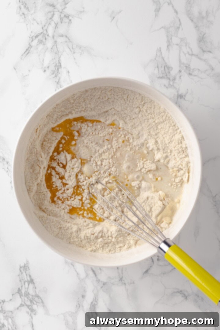 Overhead shot of wet ingredients being whisked into a bowl of dry ingredients to form the donut dough.