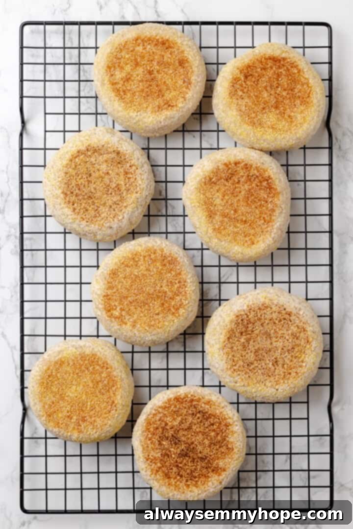 This homemade gluten-free English muffin recipe is tender, golden, and perfect for adding your favourite jam or spread. They're vegan too! Freshly cooked gluten-free English muffins cooling on a wire rack.