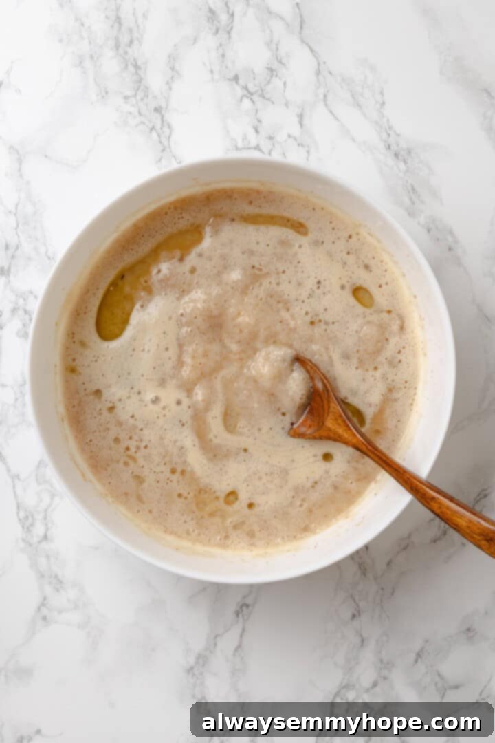 This homemade gluten-free English muffin recipe is tender, golden, and perfect for adding your favourite jam or spread. They're vegan too! Mixing bowl with wet ingredients (yeast mixture, almond milk, olive oil, psyllium gel) for English muffins.