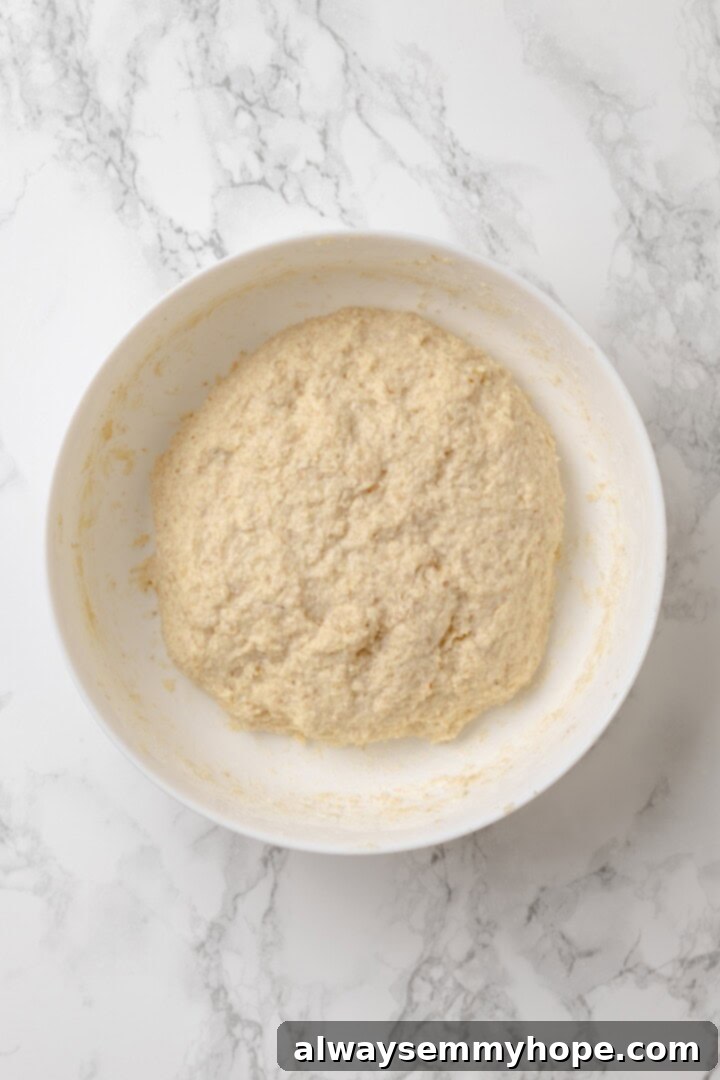 This homemade gluten-free English muffin recipe is tender, golden, and perfect for adding your favourite jam or spread. They're vegan too! Close-up overhead view of the thick, sticky dough for gluten-free English muffins in a mixing bowl.