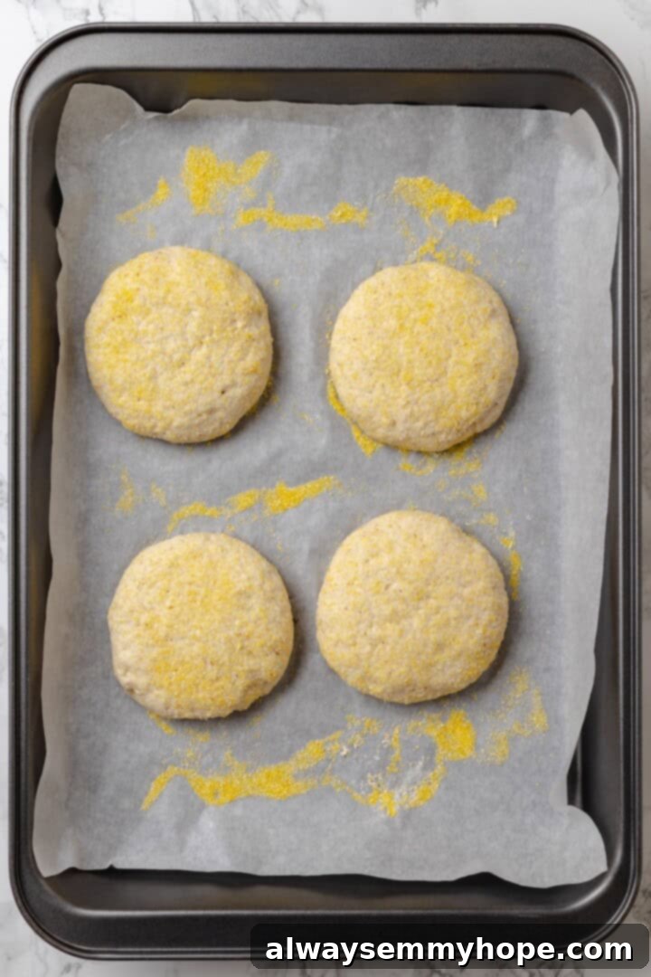 This homemade gluten-free English muffin recipe is tender, golden, and perfect for adding your favourite jam or spread. They're vegan too! Shaped gluten-free English muffin dough rounds dusted with cornmeal on a baking sheet.