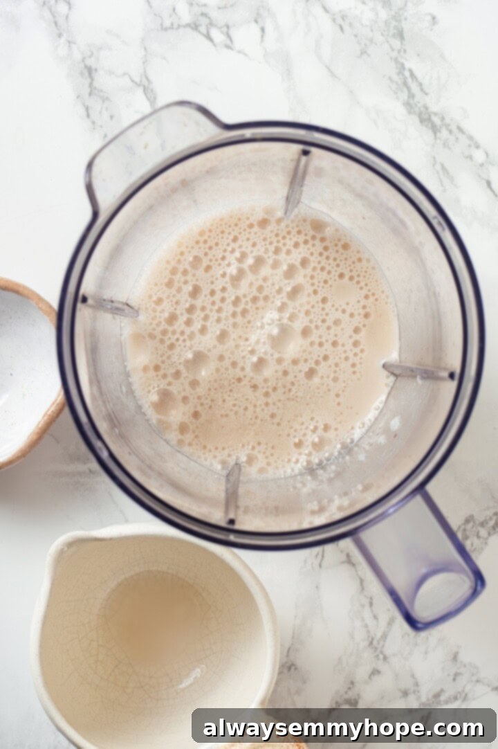 Overhead view of vegan buttermilk mixture in blender, with almond milk and apple cider vinegar combined, appearing slightly curdled and thickened