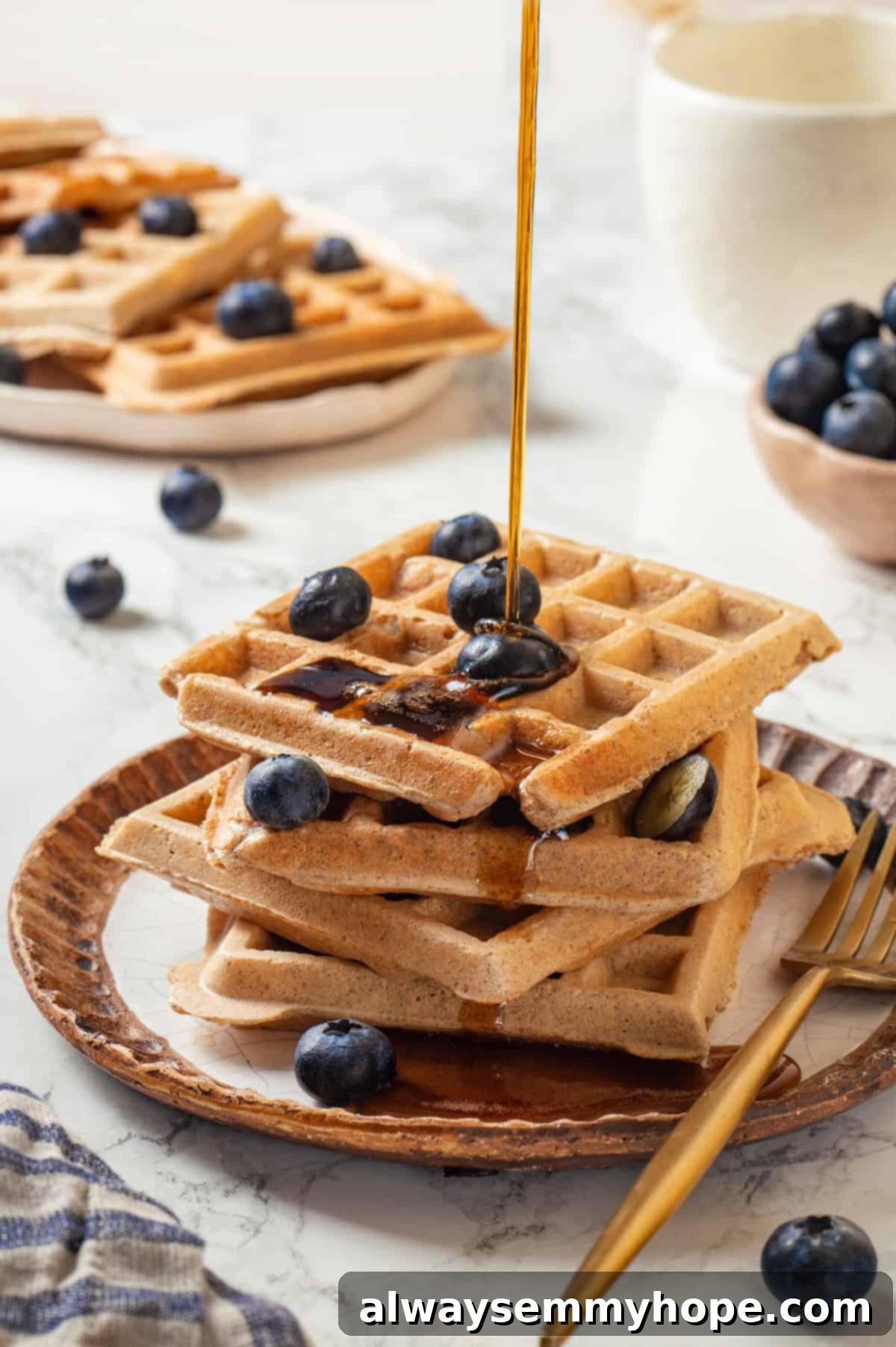 Pouring maple syrup onto a stack of golden brown protein waffles topped with fresh blueberries, showcasing a delicious and healthy breakfast