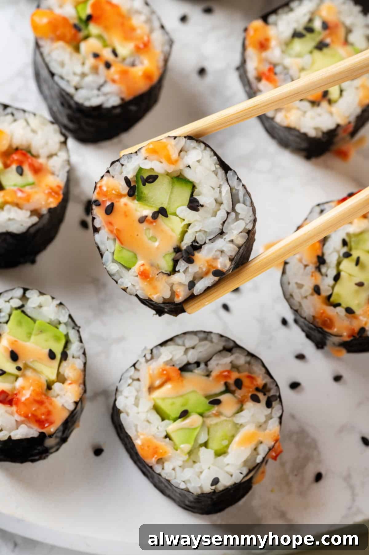 Chopsticks holding avocado sushi roll with bang bang sauce