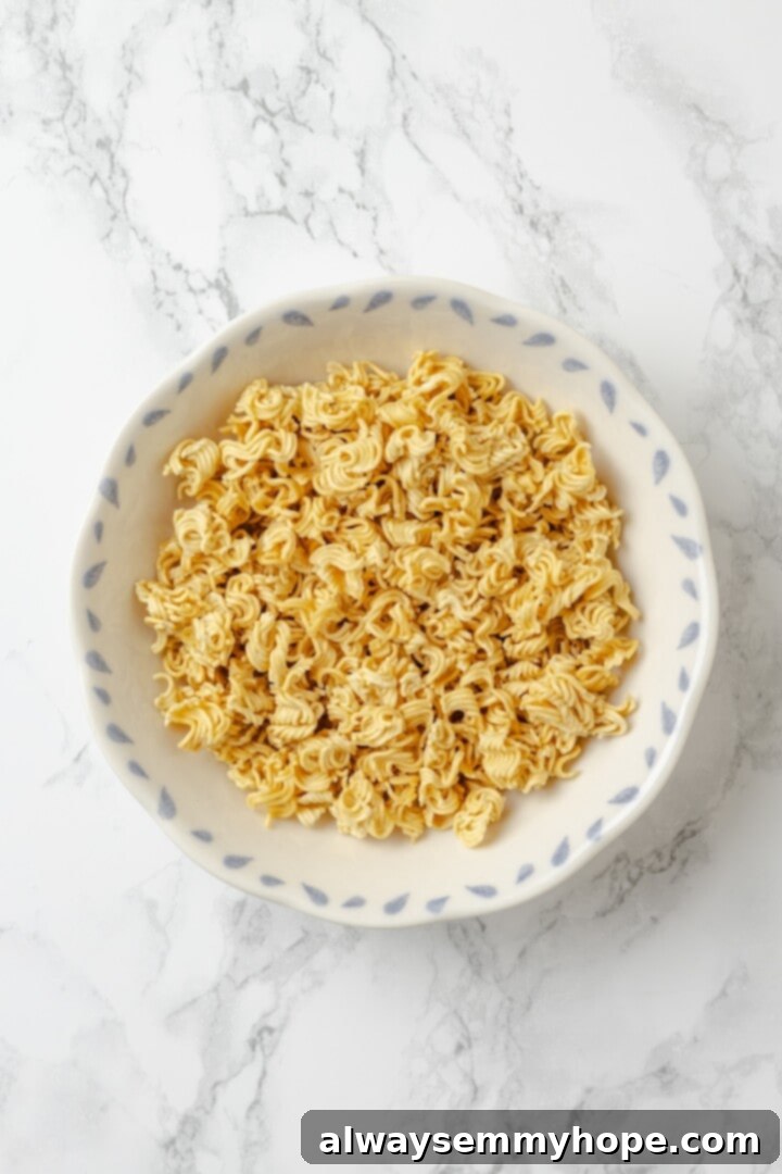 Overhead view of ramen noodles broken into small, bite-sized pieces in a mixing bowl, ready for the salad