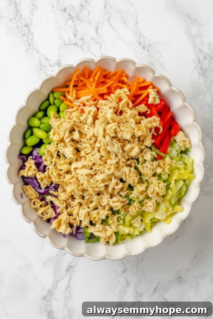 Overhead view of all salad ingredients (ramen, cabbage, edamame, carrots, bell pepper, green onions, cilantro) in a large mixing bowl before tossing with dressing