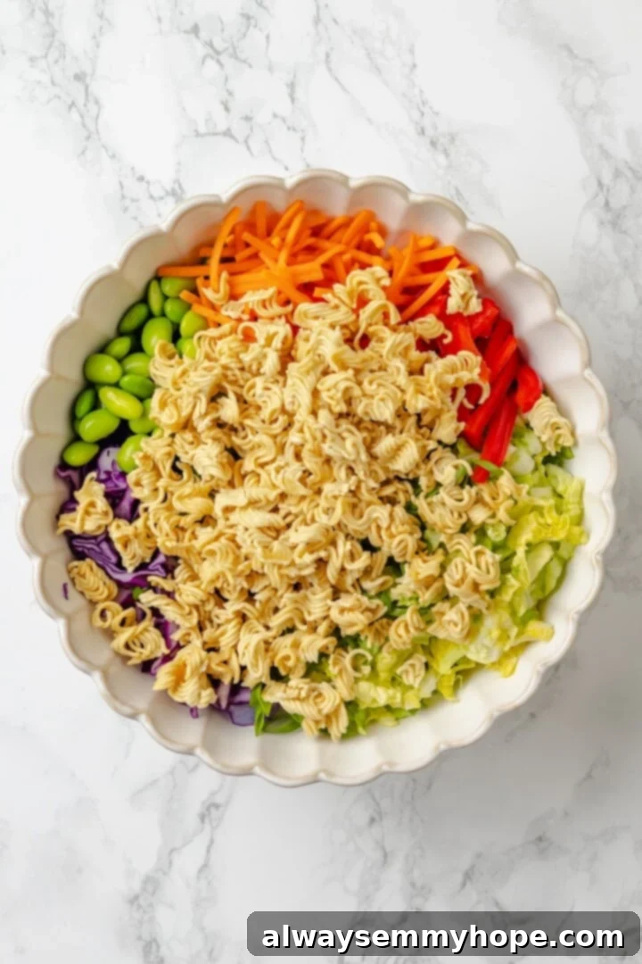 With crunchy noodles, almonds, cabbage and tender edamame in a zippy ginger dressing, this ramen noodle salad recipe is easy and delicious! Overhead view of ingredients for ramen noodle salad in bowl before tossing