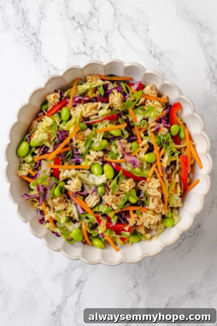 Overhead view of the ramen noodle salad in a mixing bowl with the ginger dressing poured over it, before being tossed