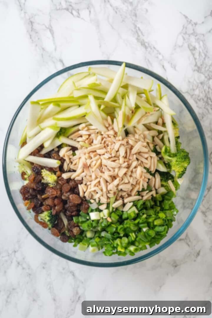 This easy broccoli slaw recipe is crisp and crunchy, sweet and savory, with a creamy dressing so good, you’ll want to eat it with a spoon! Overhead view of ingredients for broccoli slaw in bowl before tossing