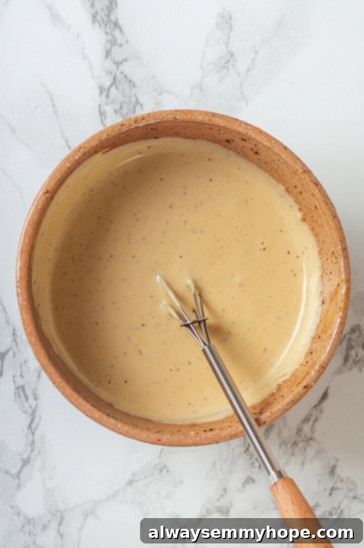 This easy broccoli slaw recipe is crisp and crunchy, sweet and savory, with a creamy dressing so good, you’ll want to eat it with a spoon! Overhead view of broccoli slaw dressing in bowl with whisk