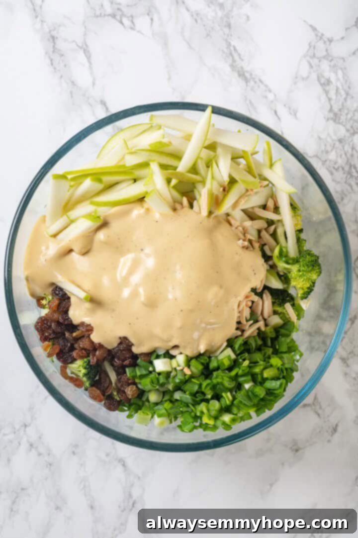 This easy broccoli slaw recipe is crisp and crunchy, sweet and savory, with a creamy dressing so good, you’ll want to eat it with a spoon! Overhead view of broccoli slaw ingredients in bowl before tossing