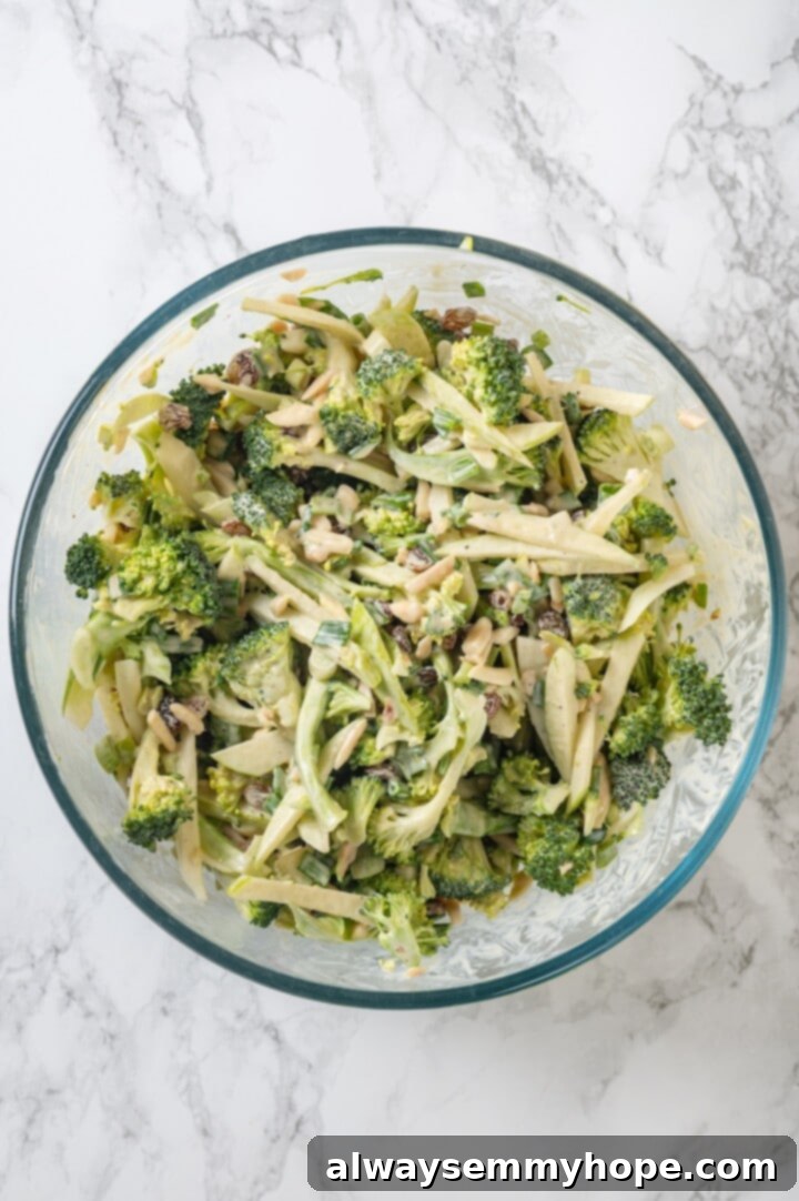 This easy broccoli slaw recipe is crisp and crunchy, sweet and savory, with a creamy dressing so good, you’ll want to eat it with a spoon! Overhead view of broccoli slaw in glass mixing bowl