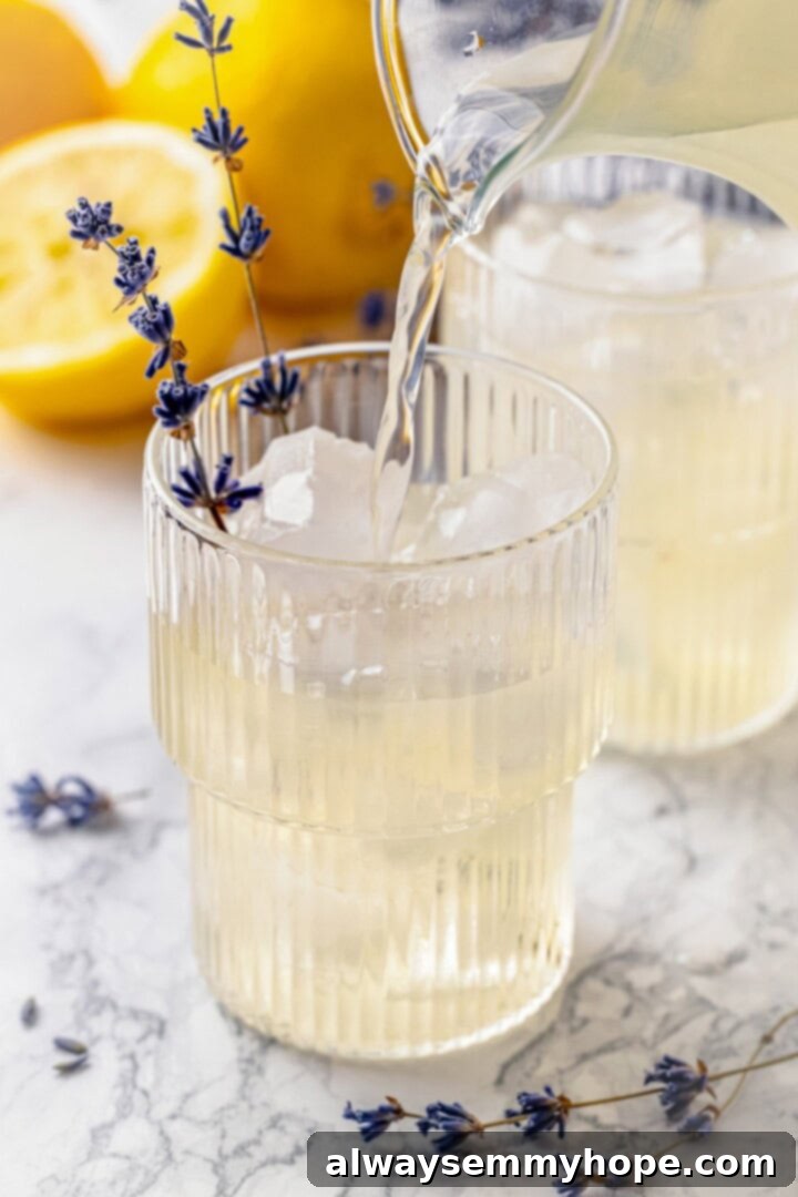 Pouring lavender lemonade into a glass filled with ice and garnishes