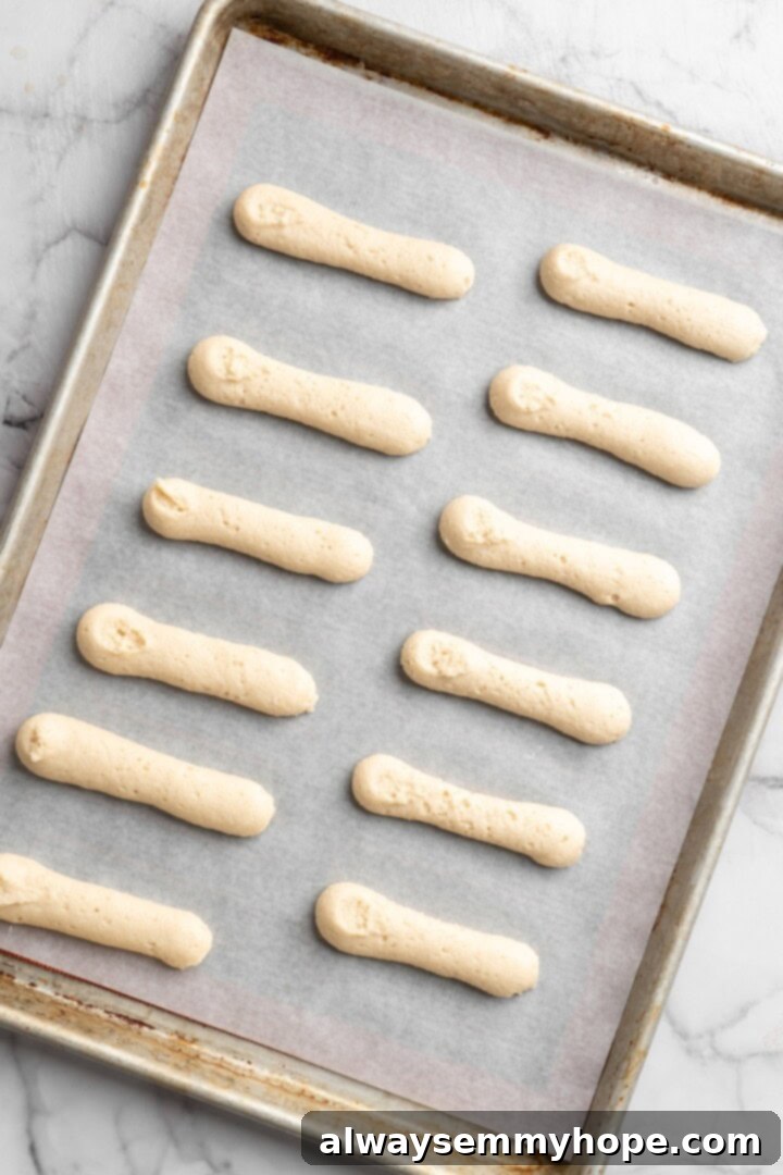 Overhead view of unbaked vegan ladyfingers on parchment-lined sheet pan