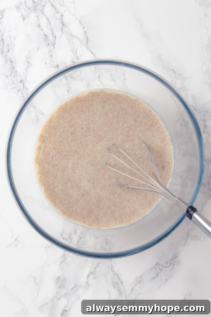 This baked oatmeal recipe is an easy meal prep breakfast! It's hearty and wholesome, with juicy berries and crunchy walnuts in every bite. Overhead view of almond milk, maple syrup, coconut oil, vanilla, and flax egg whisked in a glass mixing bowl