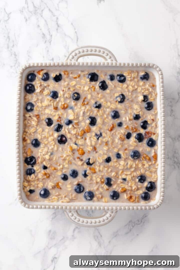 This baked oatmeal recipe is an easy meal prep breakfast! It's hearty and wholesome, with juicy berries and crunchy walnuts in every bite. Overhead view of oatmeal and blueberry mixture poured into a baking dish before baking