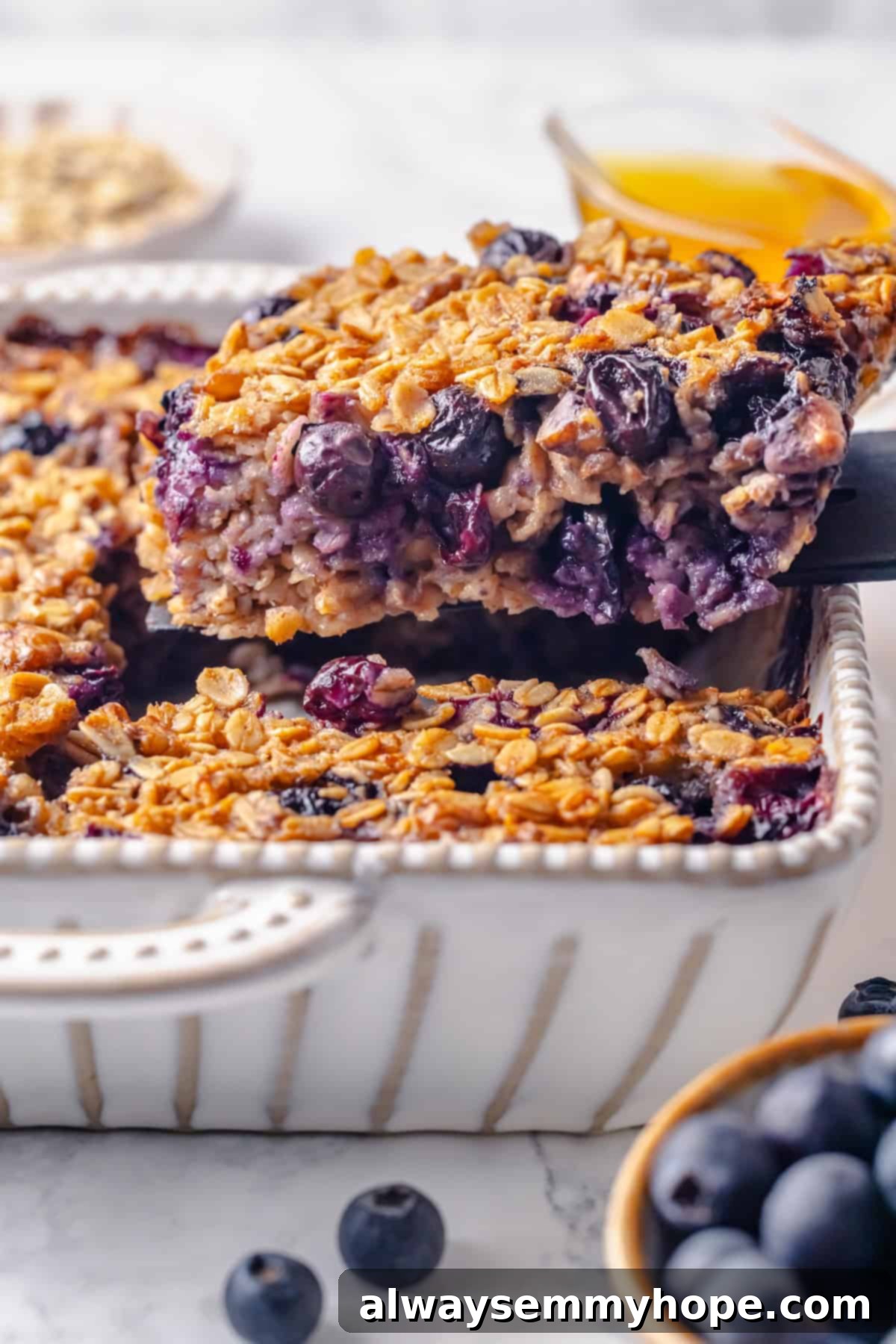 This baked oatmeal recipe is an easy meal prep breakfast! It's hearty and wholesome, with juicy berries and crunchy walnuts in every bite. Lifting a square portion of baked oatmeal from a baking pan with a spatula