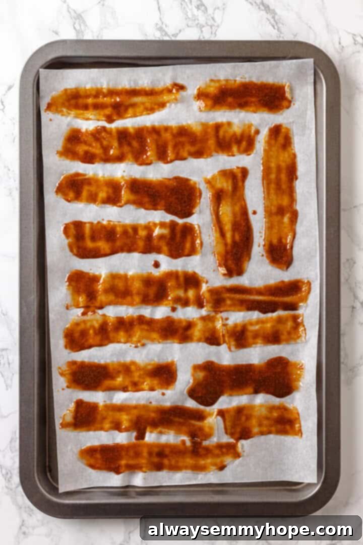 Rice paper is the secret for ultra crispy vegan bacon! This recipe is smoky, sweet, and savoury, and it's incredibly easy to make too. Overhead view of vegan rice paper bacon on parchment-lined baking sheet before baking