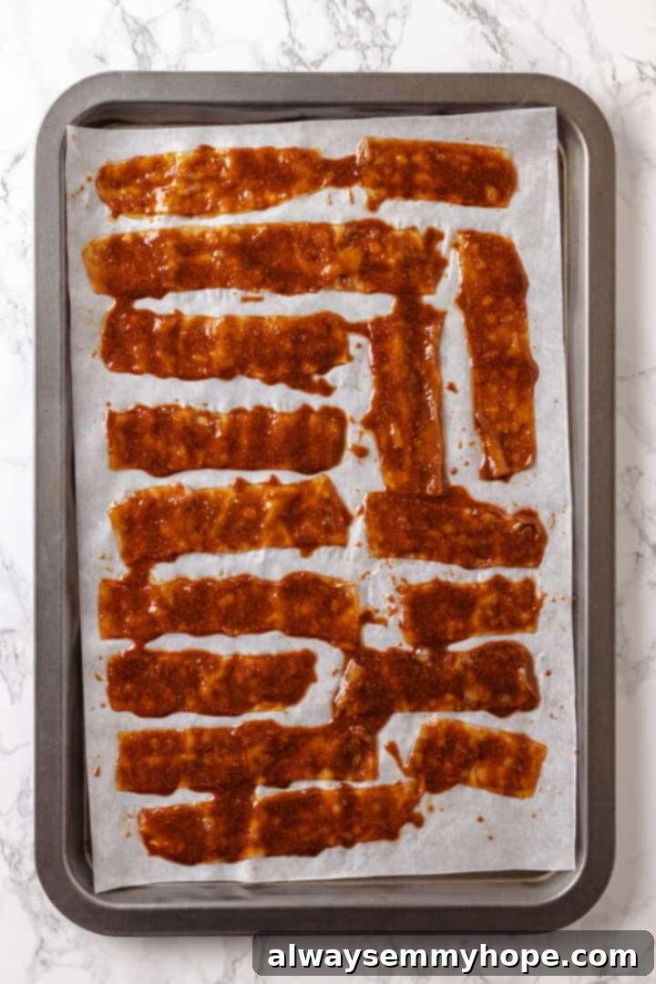Rice paper is the secret for ultra crispy vegan bacon! This recipe is smoky, sweet, and savoury, and it's incredibly easy to make too. Overhead view of vegan rice paper bacon on parchment-lined baking sheet halfway through baking