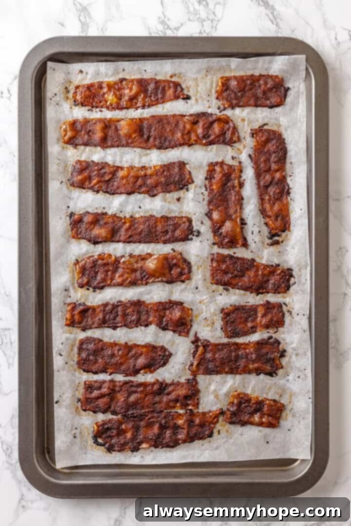 Rice paper is the secret for ultra crispy vegan bacon! This recipe is smoky, sweet, and savoury, and it's incredibly easy to make too. Overhead view of rice paper bacon on parchment-lined baking sheet