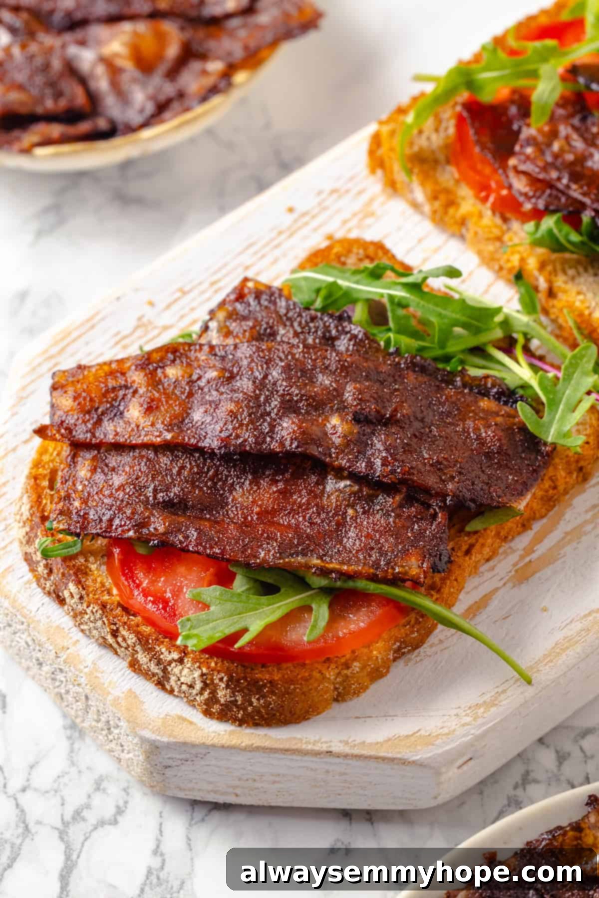 Rice paper is the secret for ultra crispy vegan bacon! This recipe is smoky, sweet, and savoury, and it's incredibly easy to make too. Crispy vegan bacon on bread with tomato and arugula
