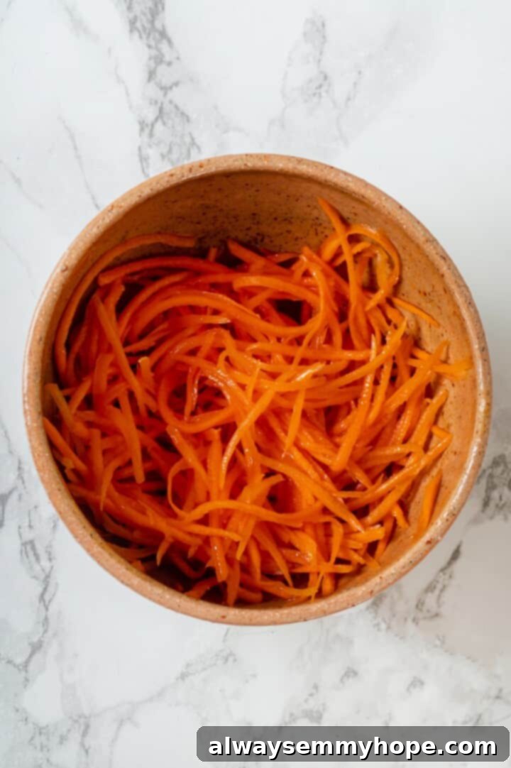 This inari sushi recipe tucks tangy sushi rice into tofu pockets with toppings like avocado, spicy carrots, and tofu scramble. Easy and fun! Overhead view of spicy carrot salad in bowl