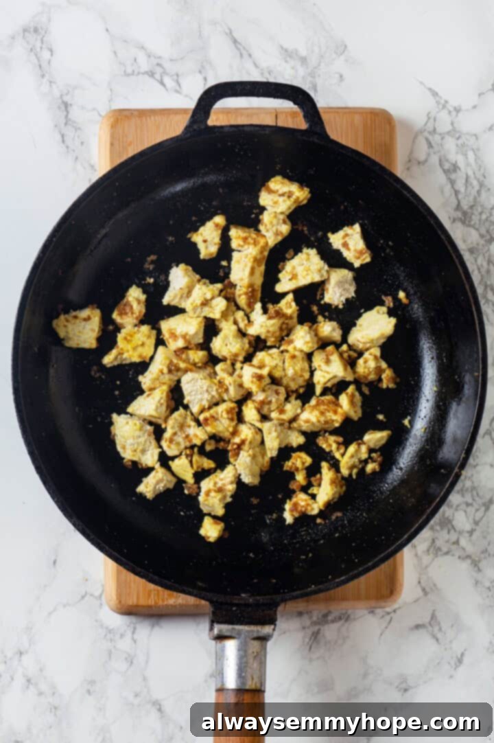 This inari sushi recipe tucks tangy sushi rice into tofu pockets with toppings like avocado, spicy carrots, and tofu scramble. Easy and fun! Overhead view of tofu scramble in skillet