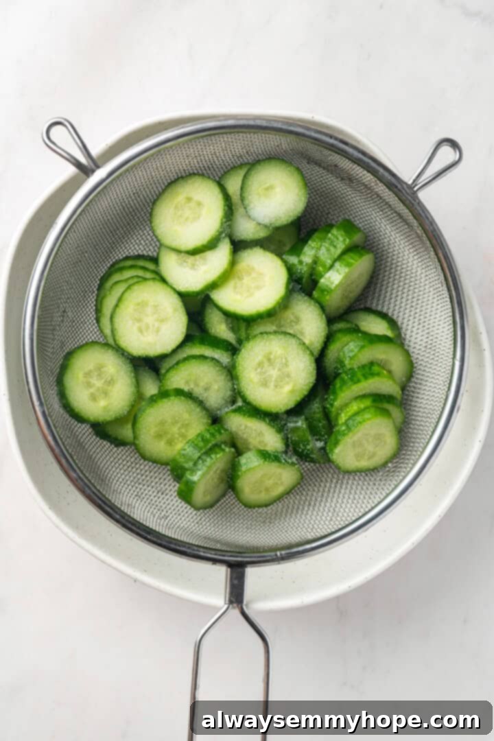 Crisp, refreshing, and full of bold flavour, this spicy Korean cucumber salad recipe is an easy side dish you’ll make all summer long! Overhead view of salted cucumber slices in colander set over bowl, draining liquid